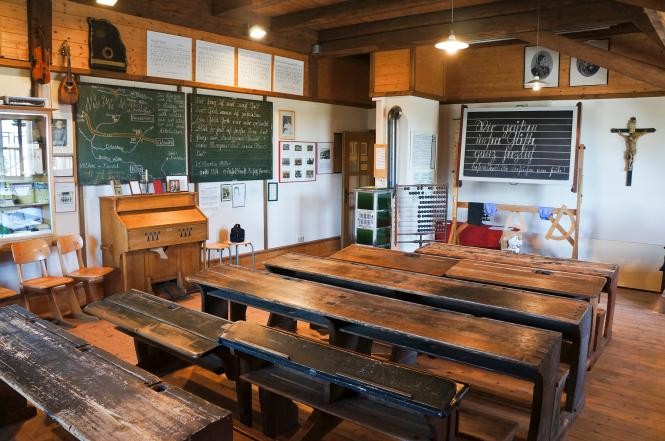 Blick in ein alts Klassenzimmer mit Holzbänken und grünen Schiefertafeln an den Wänden
